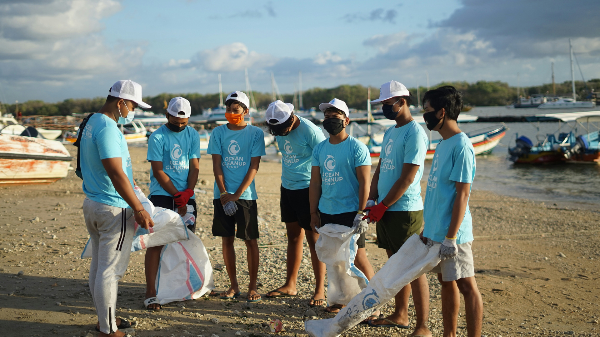 A group of volunteers standing on a beach with trash bags, doing a garbage clean up. 