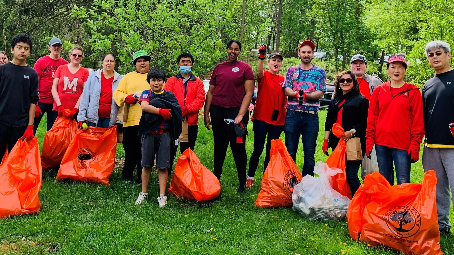 A group of volunteers are posing, smiling with bags of trash they cleaned up from a local park. 