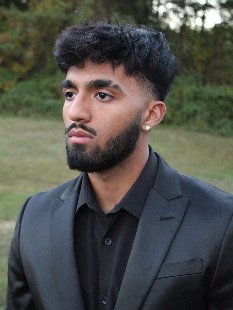 Maair's headshot features a man looking off frame to the left. He's wearing an all back suit and shirt.