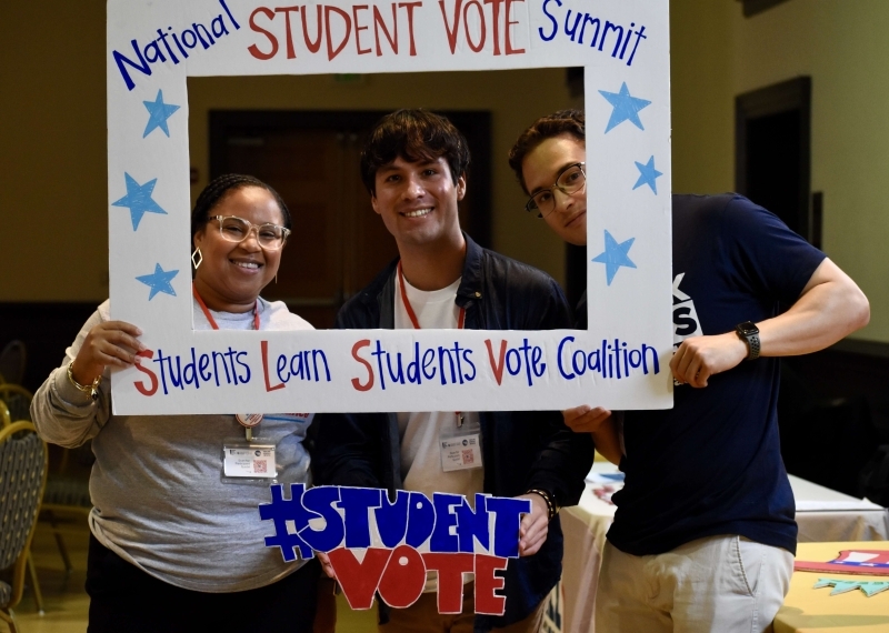students holding up a frame that says "National Student Vote Summit" and "Students Learn Students Vote Coalition" and a sign that says "Students Vote"