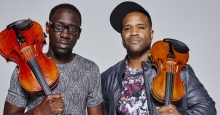 Image of musical duo "Black Violin," depicts two men holding violins on their shoulders
