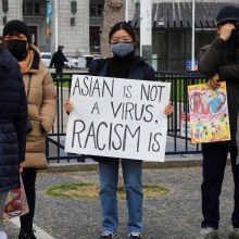 A photo of a person holding a sign that says "Asian is Not a Virus, RACISM Is"