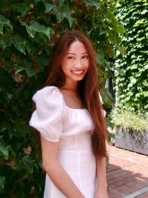Jasmine Flores headshot. She stands in a pink dress with red hair. The background is filled with green shrubbery.