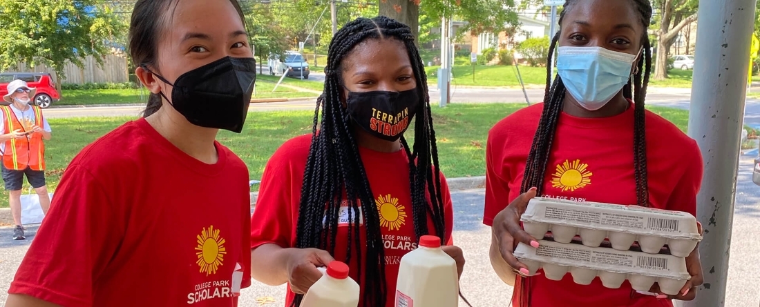 Three students wearing Maryland red carrying groceries