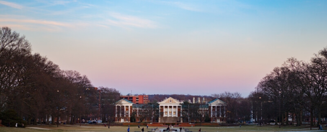 View of the Mall at dusk looking towards Miller Administration Building with students walking; small amount of snow on the grass under the trees.