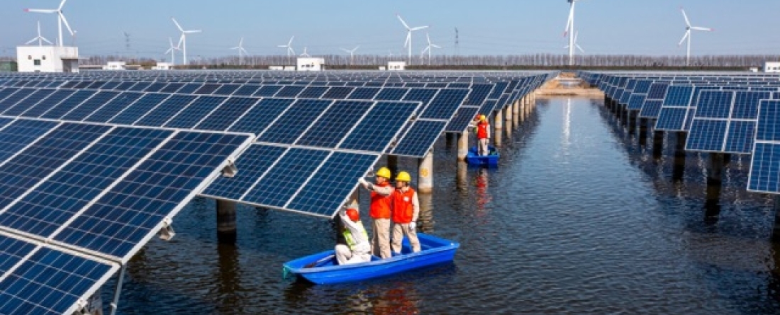 picture of workers inspecting solar panels with a wind farm in the background
