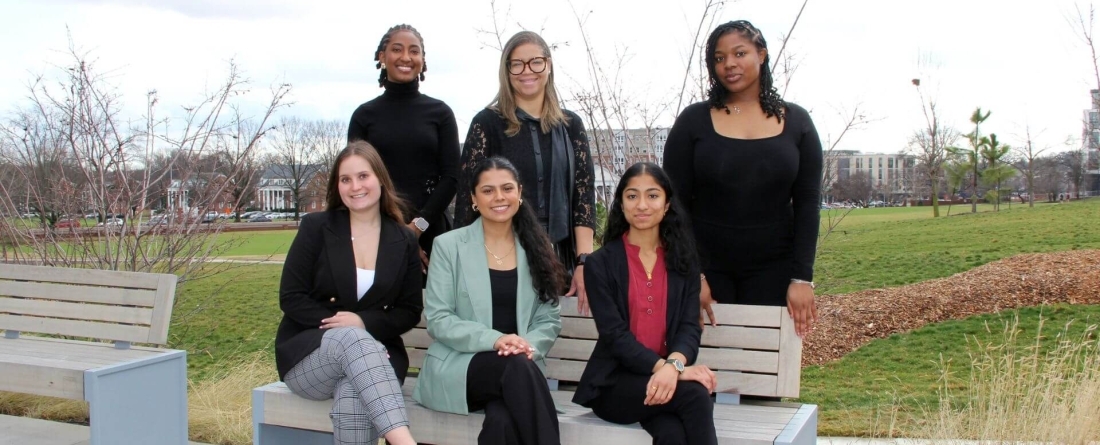 New Pizzigati fellows pose at a bench with Brandi Slaughter outside at campus entrance to Thurgood Marshall Hall