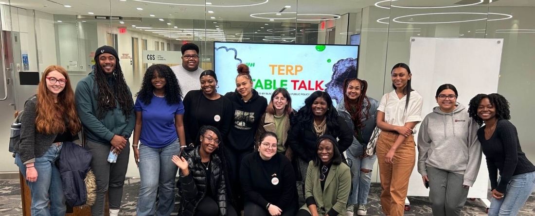a group of students stands in front of a tv screen that says "Terp Table Talk"
