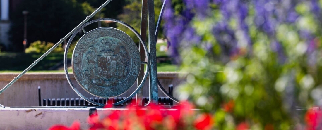 image of sundial in background with red and purple flowers in foreground.