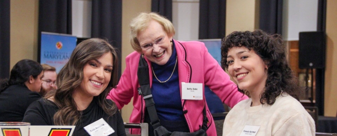 students pose with Betty Duke while seated at a table