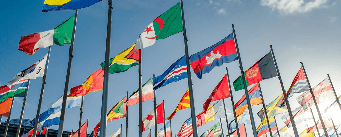 International flags fly on a clear day with blue skies and clouds.
