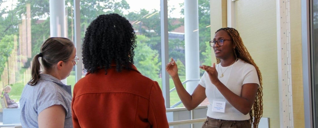 image of 3 students talking in front of a window