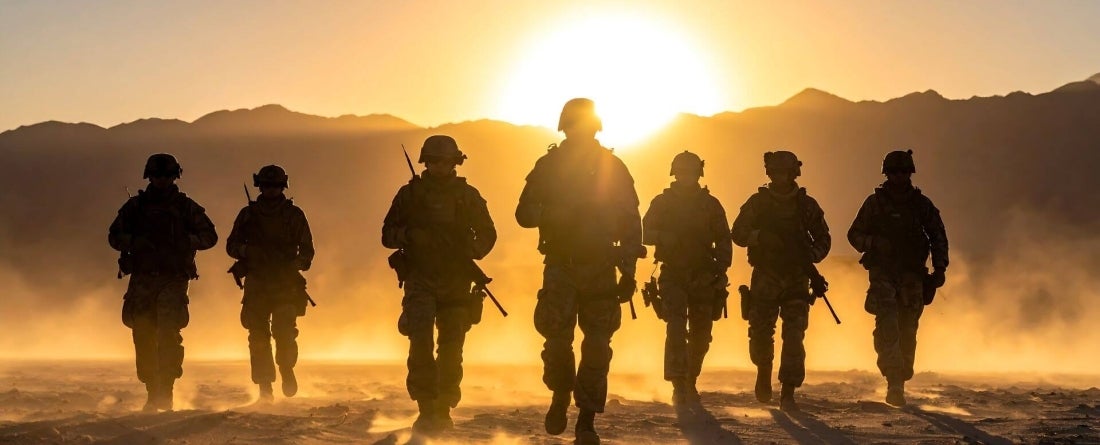 sunset silhouette image of troops in the dessert walking toward a setting sun