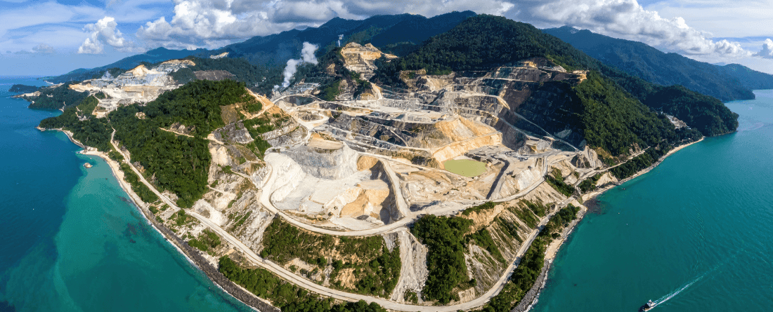 An aerial view of an island mining site surrounded by water and forested mountains.