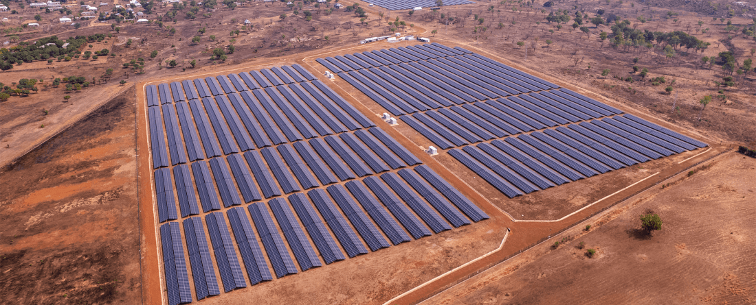 An aerial view o several solar panels lined up in two columns in a sub-saharan environment.