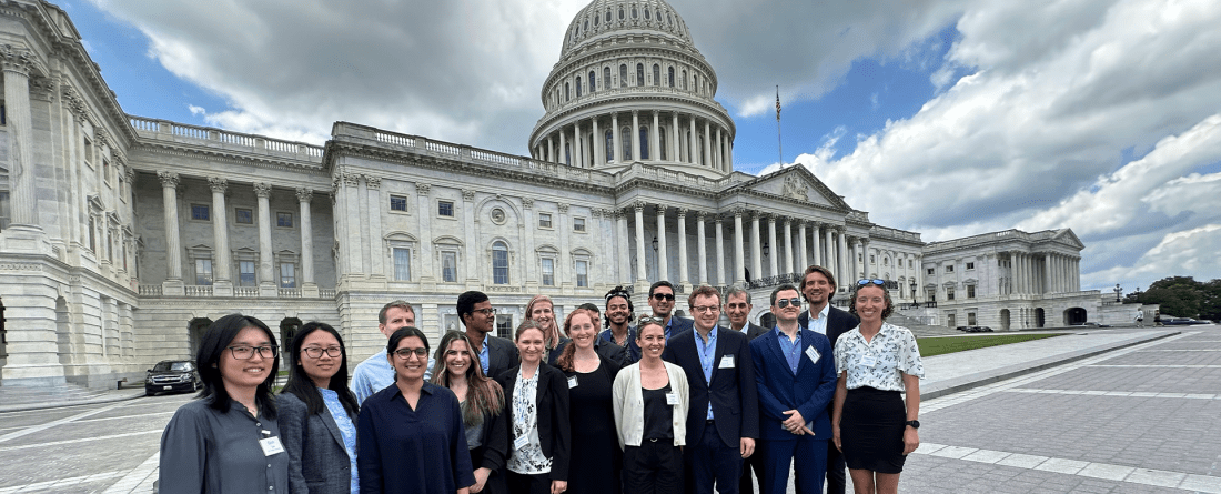 A group of people in professional clothing stand in front of a large government building.