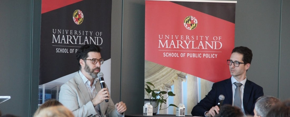 Josh Shifrinson and Daniel Immerwahr sit in front of red and black UMD School of Public Policy banners