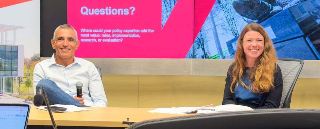 Stéphane Carcillo, head of the Jobs and Income Division at the Organisation for Economic Co-operation and Development (OECD), and Sarah Newman, an SPP doctoral student and senior researcher at the American Institutes for Research (AIR) sit at table in front of screen with red background that says "Questions? Where could your policy expertise add the most value: rules, implementation, research, or evaluation?"