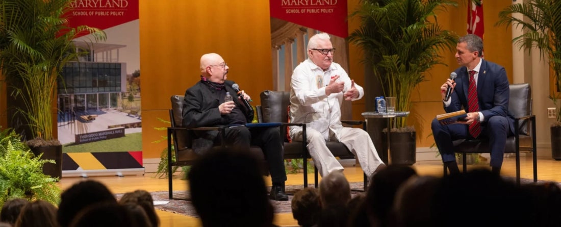 Former President of Poland and Nobel Peace Prize recipient Lech Wałęsa (center) and his interpreter (left) speak with School of Public Policy Dean Gustavo Flores-Macías on state with UMD School of Public Policy banners and plants behind them.